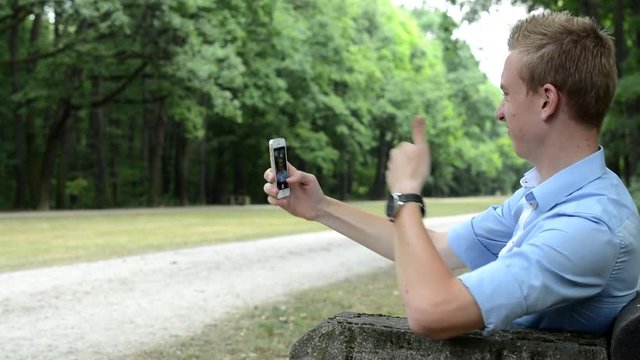 Young cheerful man sits and does a selfie in the park