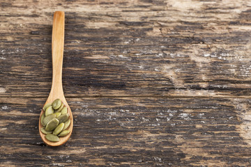 Pumpkin seeds and spoon wood on wooden background