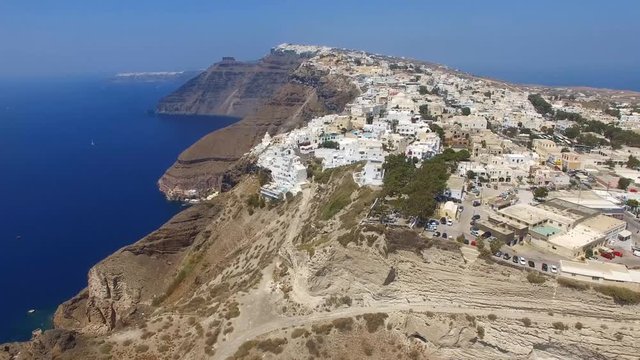 Aerial footage of Fira, Santorini - Famous white houses and blue domes on the edge of the cliff and blue lagoon.