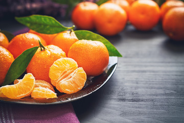 Fresh clementines with leaves served on plate, on black wooden table. Copy space