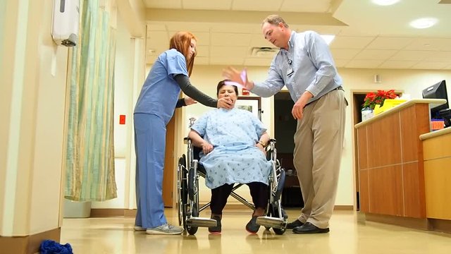 nurse and doctor discussing patient care with patient in wheelchair in hallway of hospital
