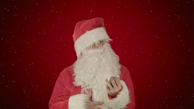 Santa claus reads and sends text messages from his cell phone  on red background with snow