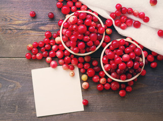 Fresh juicy cranberry in wooden round bowls and white card with the inscription on a table, close up