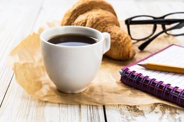 French croissant, glasses, cup of coffee and notebook