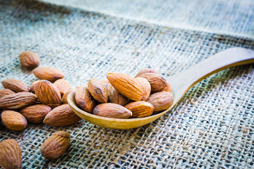 Almonds in wooden spoon place on hemp background