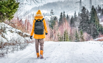 traveler with a backpack walking on snow covered road in winter forest