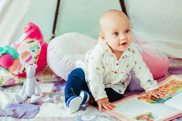 The small baby sits near toys and book