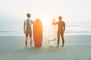Young surfers waiting the waves on beach with back sunlight 