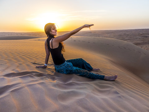 Oman, Al Raka, young woman sitting on a desert dune in Rimal Al Wahiba desert