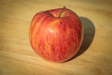 Apple shadow stretching out onto a wooden cutting board. Nice and ripe and ready to be eaten.