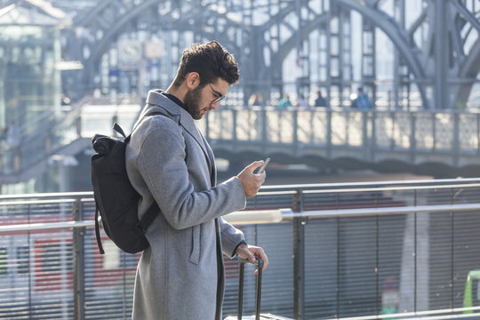 Businessman with baggage looking at cell phone at train station