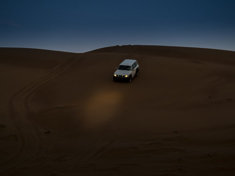 Oman, Al Raka, off-road vehicle parking on dune in Rimal Al Wahiba desert at twilight