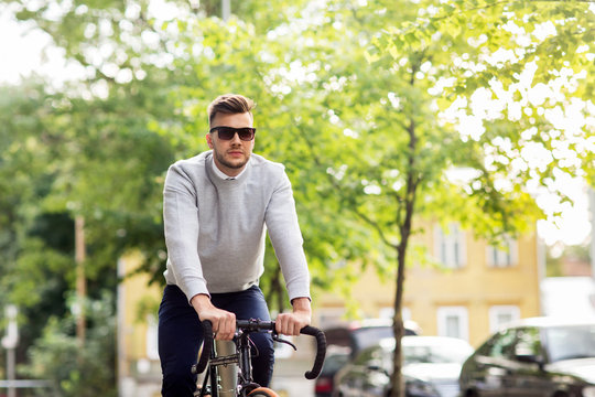young man in shades riding bicycle on city street