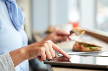 woman with tablet pc and panini sandwich at cafe