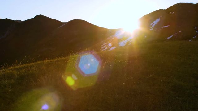 Sun rising from behind snow mountains. Tight shot with a beautiful lens flare moves through frame
