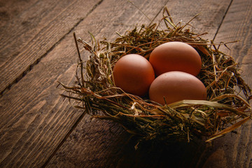 Chicken eggs in a wicker straw nest on wooden background