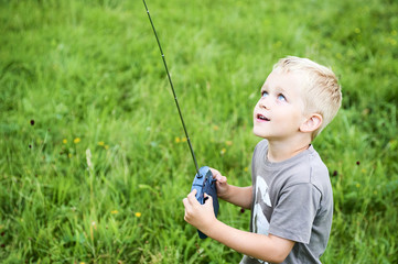 Little child blond boy playing with toy radiocontrolled airplane against green grass lawn...