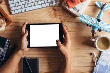 Man hands holding blank screen digital tablet and Outfit of traveler on wooden background.