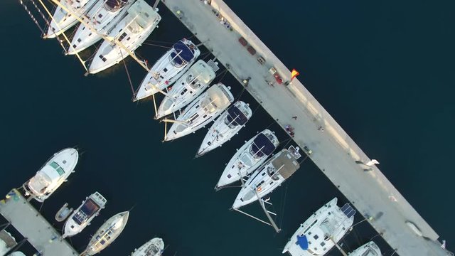 Yachts moored to pier, view from above with a quadcopter. The camera tilts down and rotates around its axis. Aerial view.