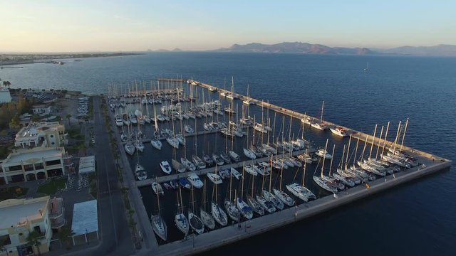 Flying around yacht marina in Kos island at sunset. Many ships moored in the cosy marina. Aerial view.