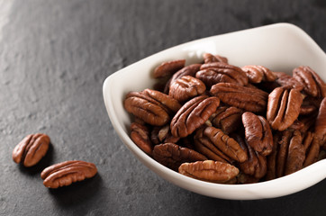 Triangular bowl full of peeled pecan nuts on a slate plate, sele