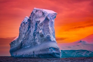 Antarctic iceberg in the snow floating in open ocean. Red sunset sky in the background. Beauty world
