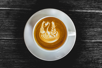 Close up white cup of Coffee, latte with beautiful latte art on the black wood background.