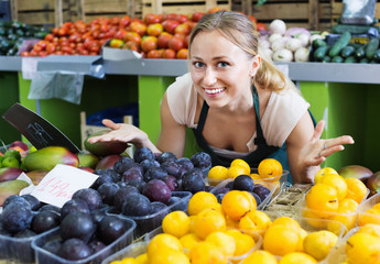 Cheerful  female seller wearing apron holding plums