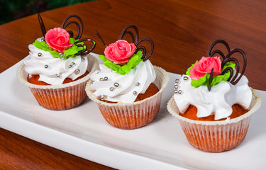 Delicious red velvet cupcakes decorated with pink rose on wooden background