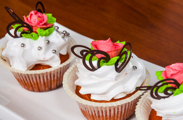Delicious red velvet cupcakes decorated with pink rose on wooden background