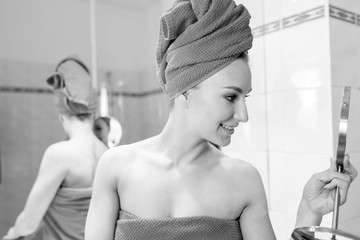 Junge Frau im Bad lächelt, sieht in den Spiegel, spiegelt sich, achtet auf ihre Haut, ihr...
