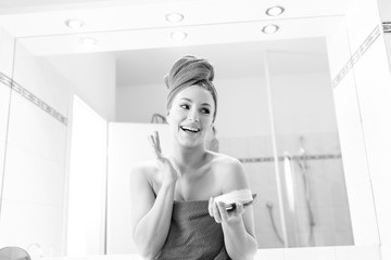 Woman looks into mirror in her bathroom and puts moisture lotion cream on her smile face