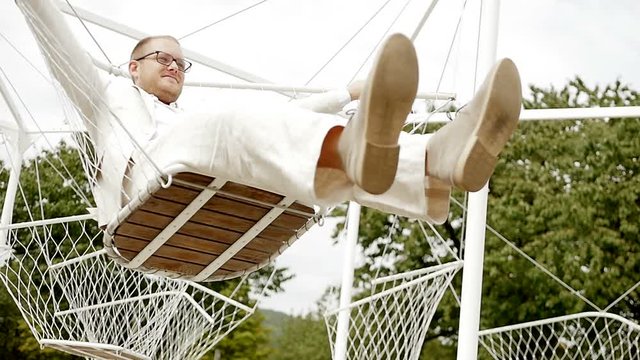 carefree man in casual white suit swinging in swing outdoors. white style background