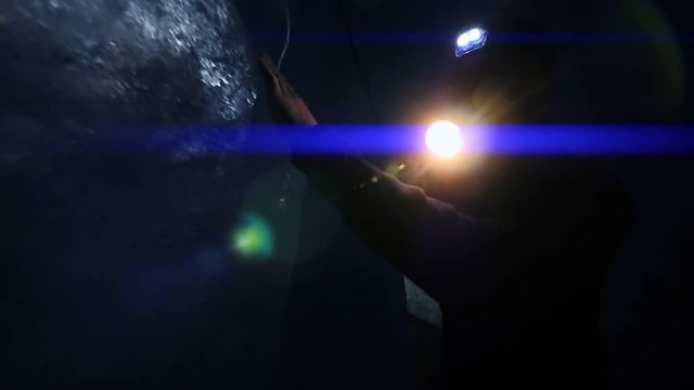 man holding flashlight touching ice inside dark glacier cave. light beam background.