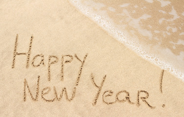 Happy New Year handwritten on sandy beach with ocean wave on background