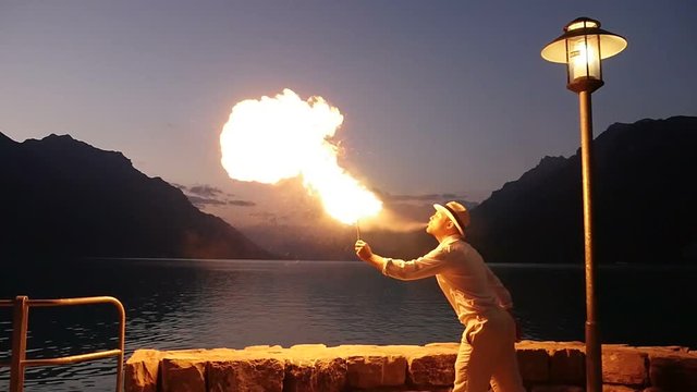 fire artist spitting fire outdoors in front of lake at night. beautiful lifestyle background