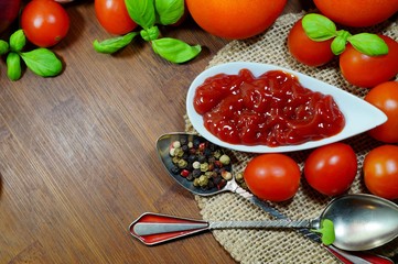Tomato ketchup sauce in a bowl with spices, herbs and cherry tomatoes. View from above.
