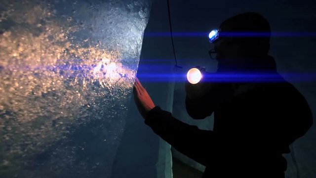 male scientist exploring ice glacier using a flashlight. blue light beam.