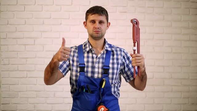 The man with the sanitary key. Plumber showing thumbs up. Plumber holding pipe wrench.