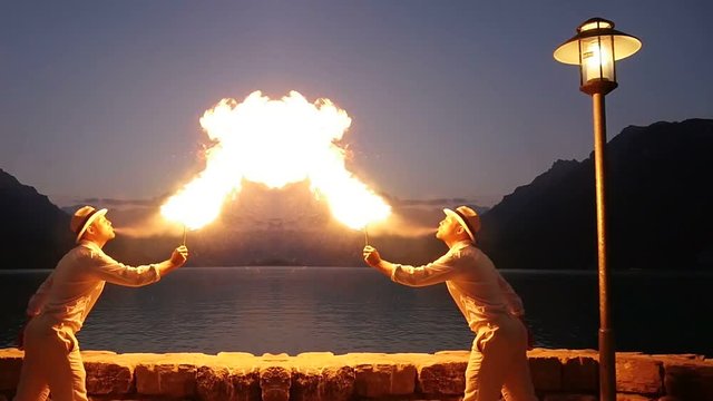 fire eater spitting fire outdoors in front of lake at night. beautiful lifestyle background