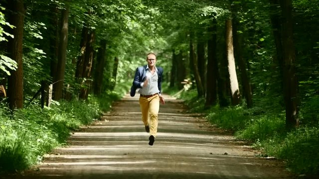 slow motion of running man facing camera. green park background.