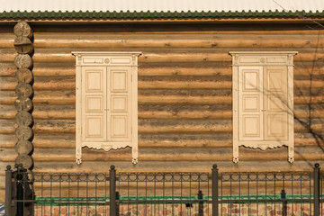 wooden wall from logs of the same flat, two shuttered windows, the kind of sunny weather in winter, roof snow, metal fence