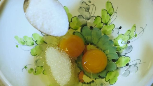 Cooking curd casseroles. Female hands adding three spoons of sugar in a dish with broken hen eggs. HD