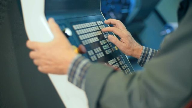 Worker hands on the control panel of a computer numerical control programmable machine.