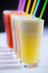 line of cold colorful variety of fruits smoothies in glasses with straws