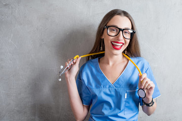 Portrait of a young nurse in uniform with stethoscope on the gray wall background