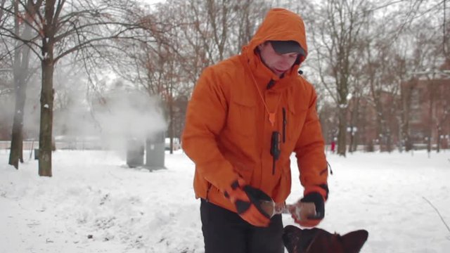 Man training shepherd dog with stick for aport in winter snow park