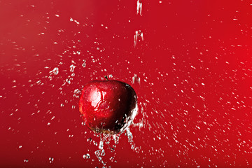 red apple under a waterfall splashing on a red background
