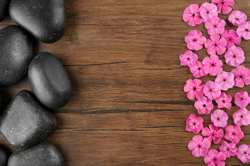 Fototapeta na wymiar Spa stones with pink flowers on wooden background, top view