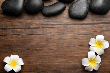 Fototapeta na wymiar Spa stones and plumeria flowers on wooden background, top view